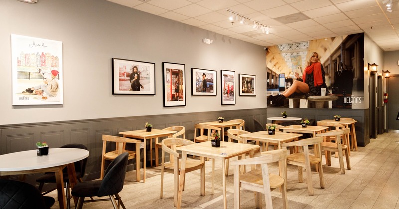Interior of a cafe with wooden tables and chairs, artwork on the walls, and potted plants on each table
