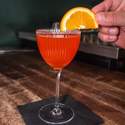 Cocktail in Nick and Nora glass being garnished with a orange slice.