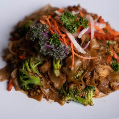 Stir-fried flat noodles with chicken, broccoli, and vegetable garnish.