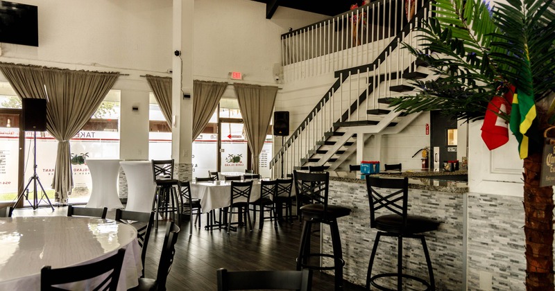 Interior view of a restaurant, circular tables, black chairs, a staircase, and a bar area