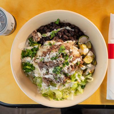 A bowl containing sliced beef, black beans, lettuce, rice, cilantro, and zucchini.