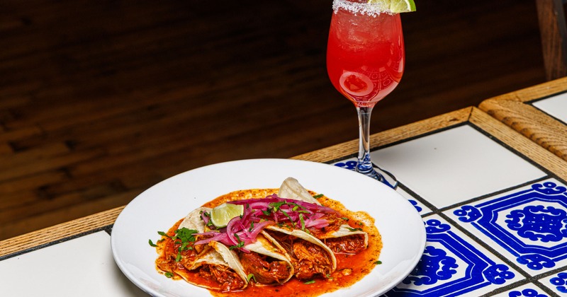 Serving of tacos alongside a cocktail in a wine glass