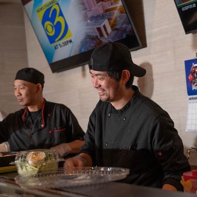Two chefs in black uniforms preparing food behind a counter.