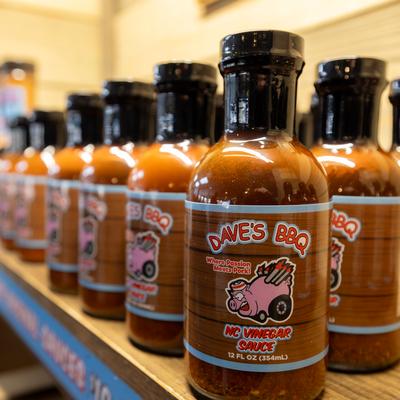Bottles of Dave's BBQ NC Vinegar Sauce on a wooden shelf.