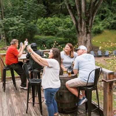 People relaxing on a wooden deck surrounded by lush green trees and string lights.