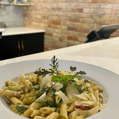 A plate of penne pasta with a creamy sauce and various garnishes in a restaurant setting..