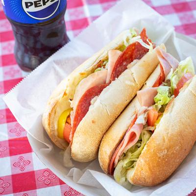 Two Italian Sub sandwiches served with a soda.