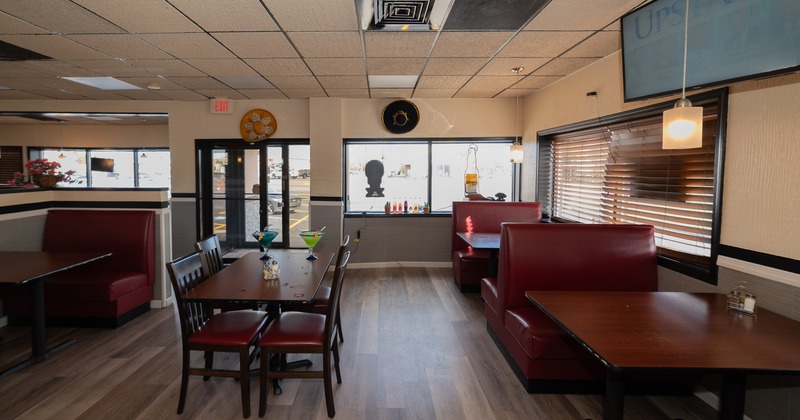 Interior with red booths, a central table with chairs and large windows with blinds.