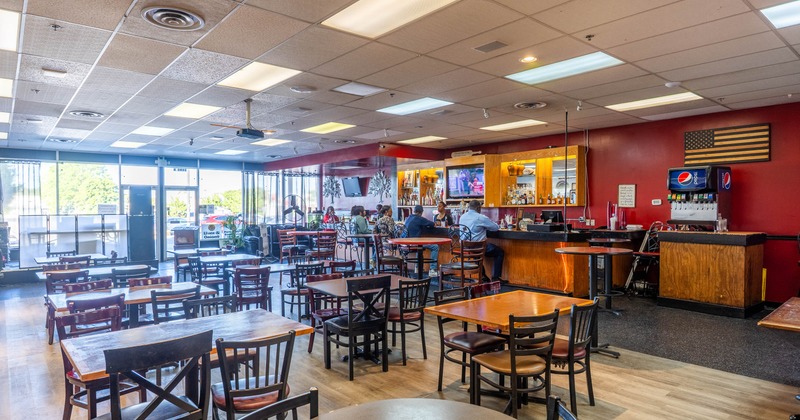 Interior of a casual dining restaurant with wooden tables, chairs, and a bar area