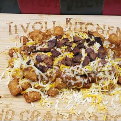 Tater tots loaded with shredded cheese and bacon bits, served on a wooden board.