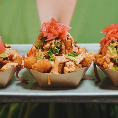 Person holding a plate with multipe portions of Loaded Tots.