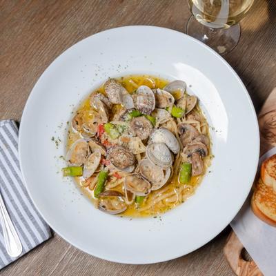 Clam linguine plate served with toast and white wine, top down view.