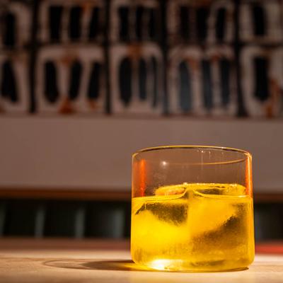 White Negroni with ice sits in a clear glass on a wooden table.