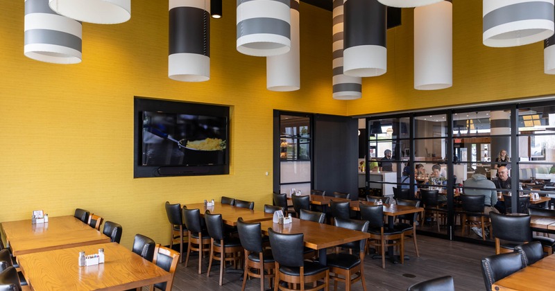 Modern restaurant interior with a bright yellow wall, wooden tables, black chairs