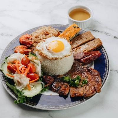 Vietnamese Broken Rice dish with grilled meats, fried egg, sauce, and fresh vegetables.