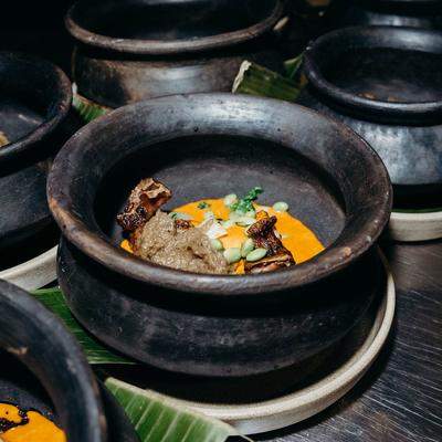 A gourmet dish with orange puree in a rustic clay pot.