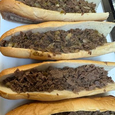 Four cheesesteak sandwiches with chopped meat and onions on hoagie rolls.