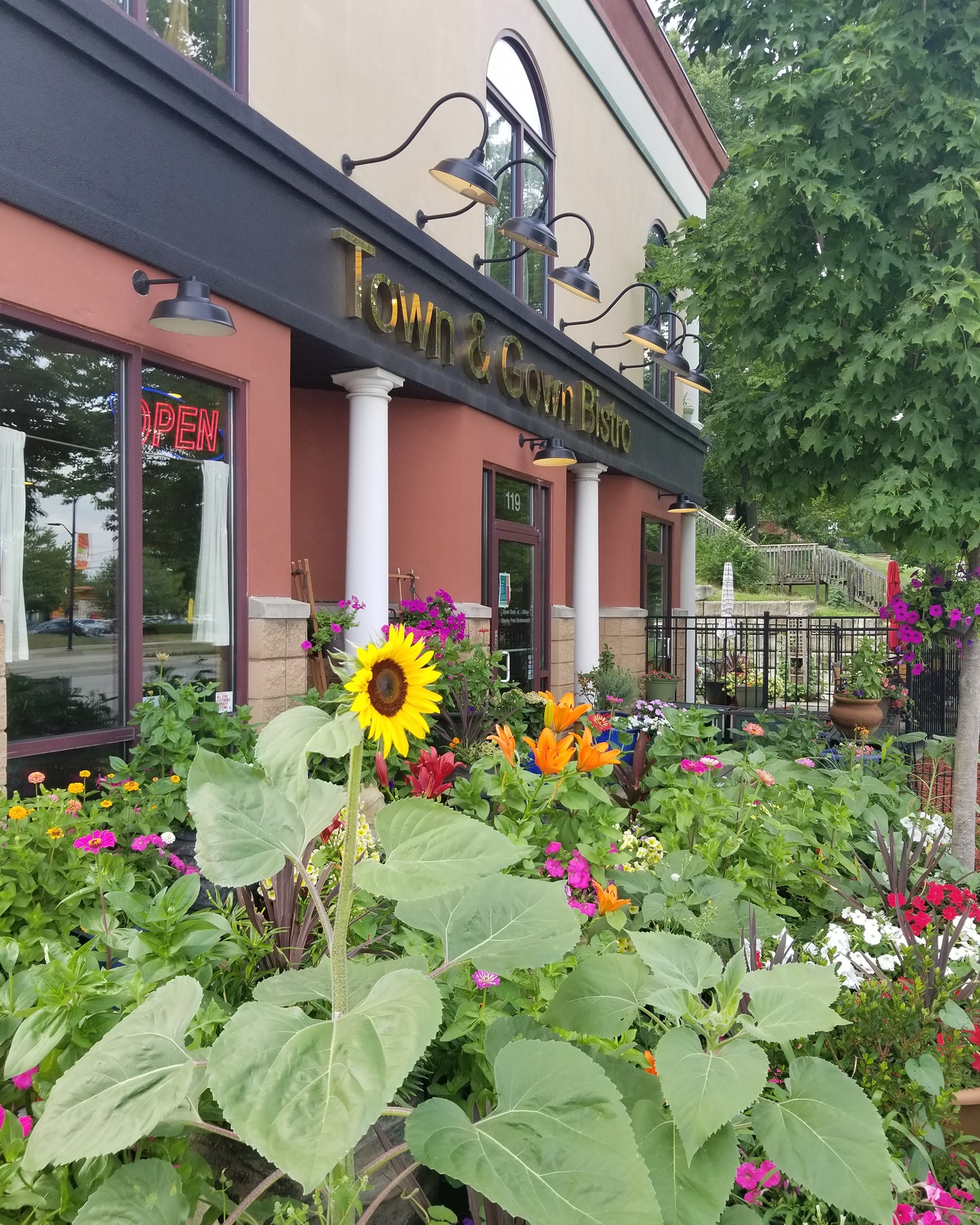 An outside photo of the front of the restaurant with many flowers including a sunflower