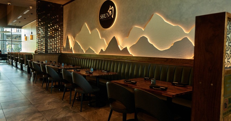 Interior, cushioned banquette, wooden tables, glowing abstract mountain wall installation