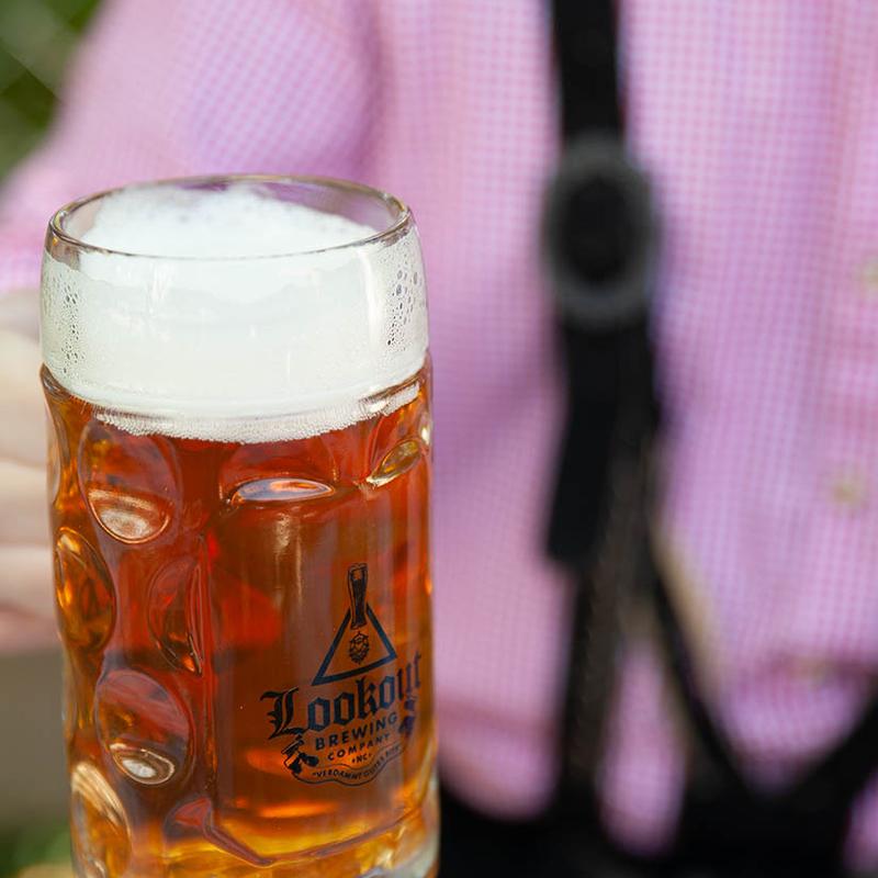 Frothy amber beer in a branded glass mug with a person in the background.
