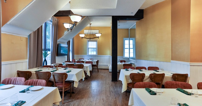 Interior of a restaurant dining area with white tablecloths, wooden chairs, and light yellow walls