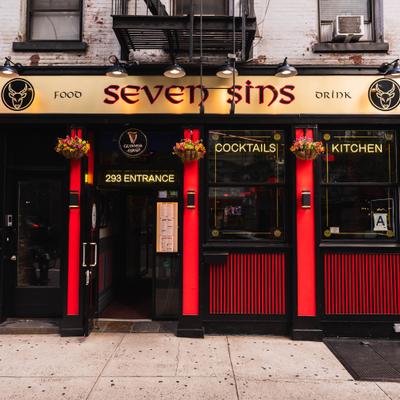 Seven Sins pub exterior storefront featuring red panels and hanging baskets of colorful flowers.