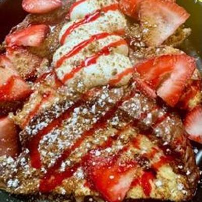 French Toast topped with fresh strawberries, powdered sugar, strawberry syrup, and whipped cream.