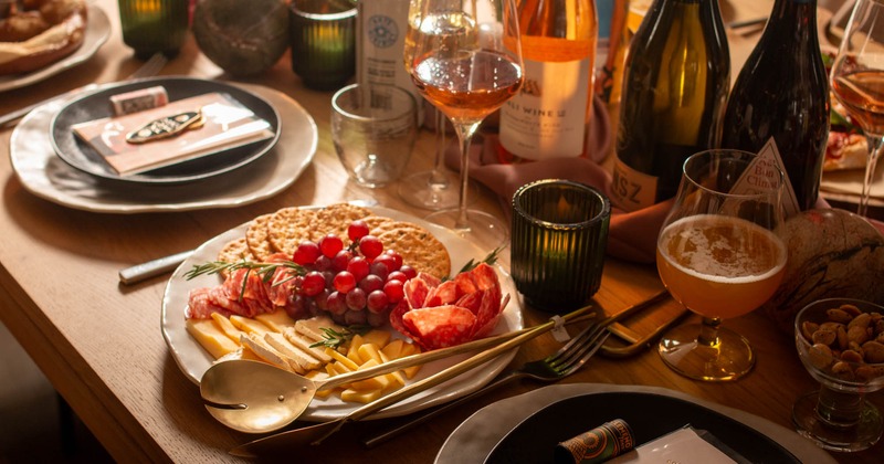 A cozy dinner table set with a charcuterie board, wine and beer glasses and bottles