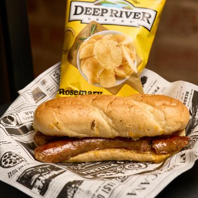 A sausage sandwich with a bag of chips.