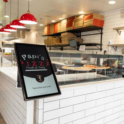 Digital ordering kiosk next to pizzas on display.