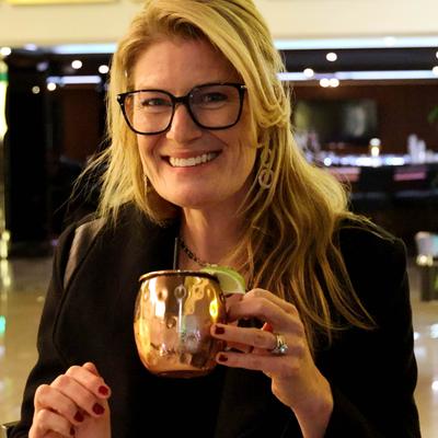 A smiling person holding a copper mug with mule cocktail.