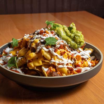 A plate of nachos topped with melted cheese, ground beef, guacamole, sour cream, and cilantro.