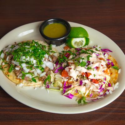 Two tacos with cilantro, onions, cabbage slaw, served with green salsa and lime.