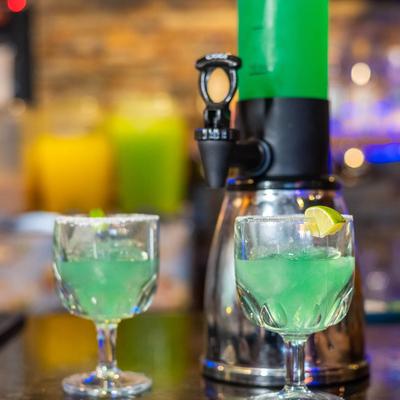 Tower Margarita served in large drink dispenser with two glasses.