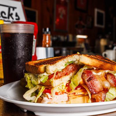 Club sandwich with bacon, lettuce, tomato, and cheese served with a soda.