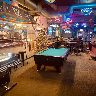 A game room with a pool table, neon signs, and a Christmas tree.