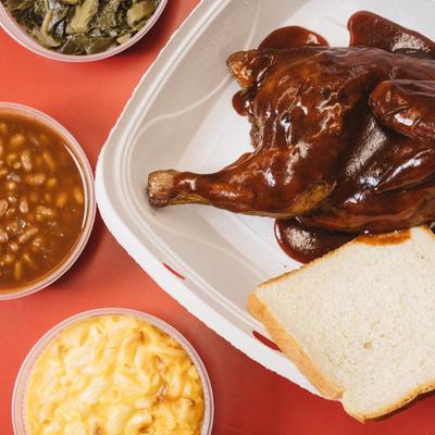 A BBQ chicken meal with sides of mac and cheese, baked beans, and collard greens.