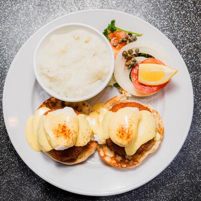 Eggs Benedict topped with hollandaise sauce served with creamy grits and garnish.
