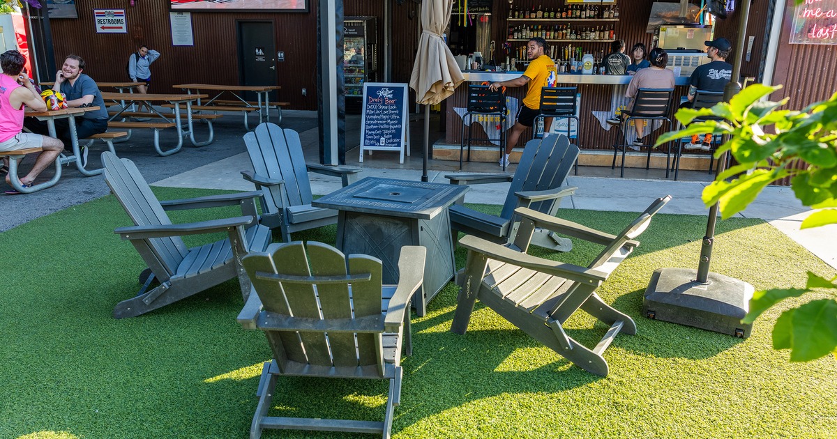 Outdoor seating area with five Adirondack chairs arranged in a circle around a square fire pit table