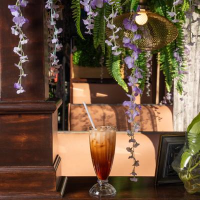 Iced  drink on wooden counter beneath hanging purple flowers and greenery.