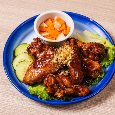 Crispy Thai-style chicken wings with sauce, fried garlic, cucumbers, and pickled veggies.