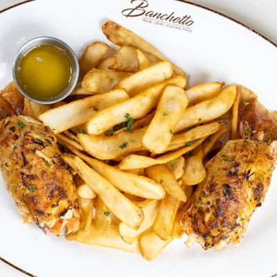 Crab-stuffed lobster tail with fries and drawn butter on a plate.