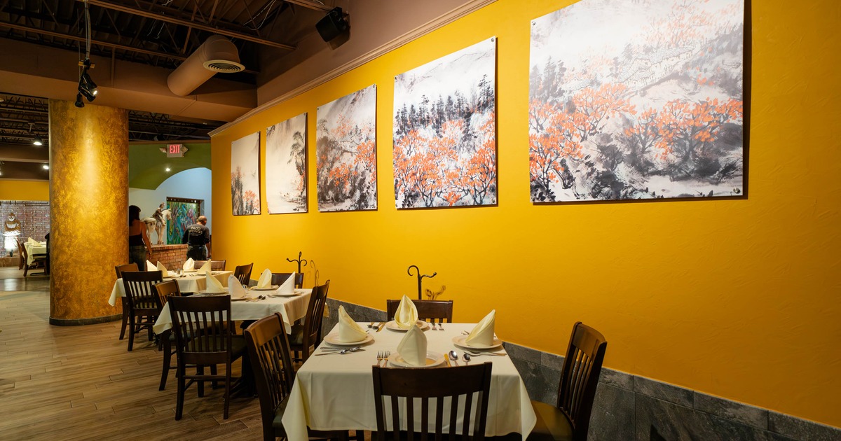 Restaurant interior with tables set for dining, yellow wall with paintings