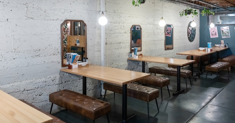 A modern and minimalist dining area with light wooden tables and brown upholstered bench seating