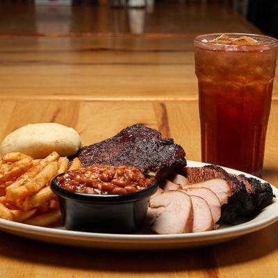 BBQ platter featuring sliced smoked meat, ribs, a side of baked beans, and fries.