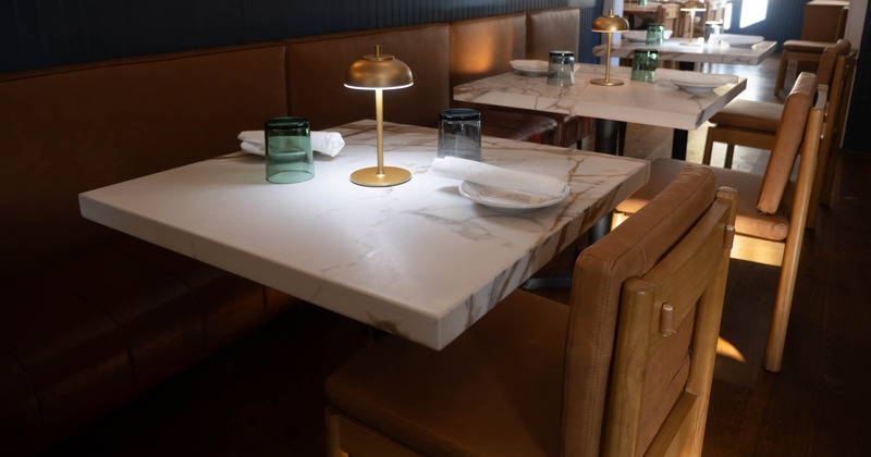 Restaurant interior with marble tables, brown leather seating, and gold table lamps