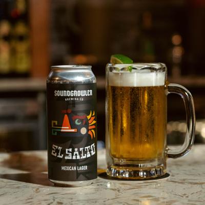 Can of beer served alongside a mug garnished with a lime wedge.