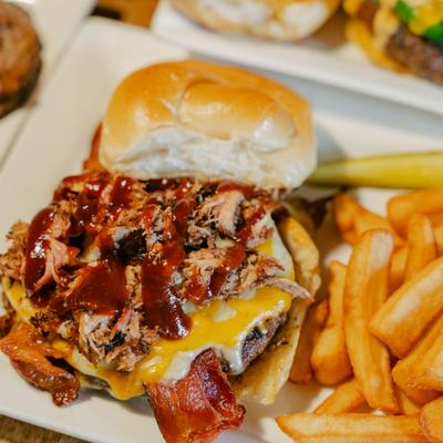 Burger topped with pulled pork, bacon, and barbecue sauce, served with fries.