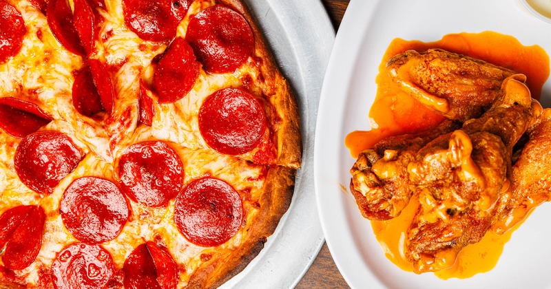 Pepperoni pizza with melted cheese served with spicy buffalo chicken wings