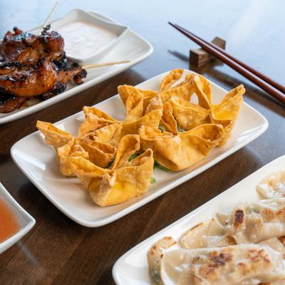 Grilled chicken skewer plate, a plate with crab wontons, a plate with potstickers.